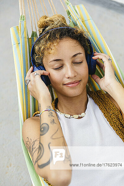 Beautiful woman with eyes closed listening music through headphones on hammock