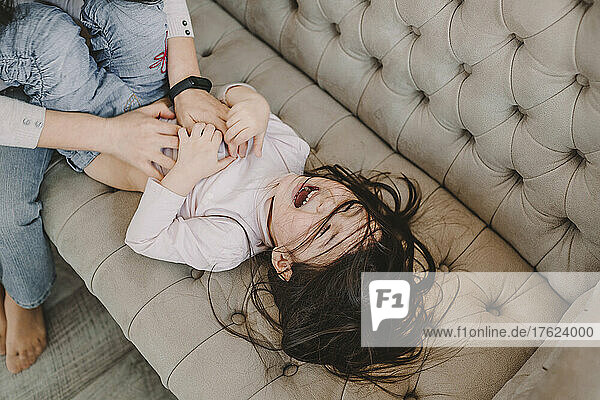 Mother tickling daughter on sofa at home