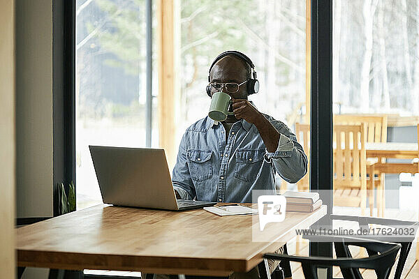 Young businessman drinking tea using laptop sitting at dining table at home