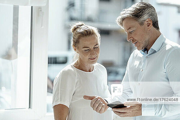 Businessman showing smart phone to businesswoman in office