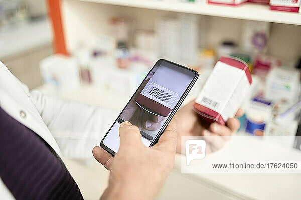 Pharmacist scanning barcode of medicine box through smart phone at pharmacy store
