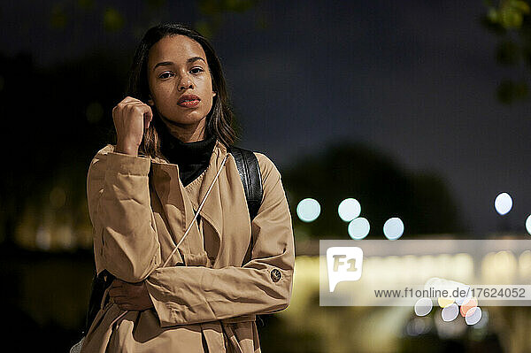 Young woman wearing coat standing outdoors at night
