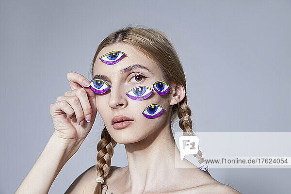 Young woman with braided hair with eyes stickers on face at studio