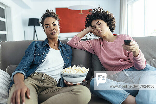 Bored women sitting together on sofa in living room at home