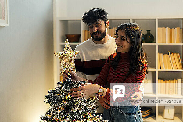 Happy couple decorating and putting star on Christmas tree at home