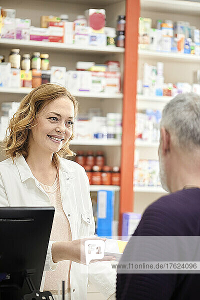 Smiling female pharmacist giving medicine to customer at checkout counter