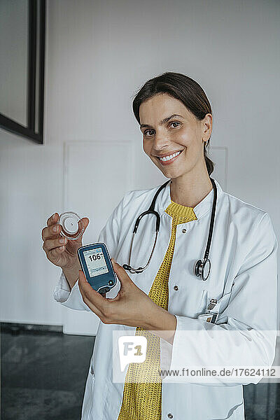 Smiling doctor holding blood glucose meter in clinic