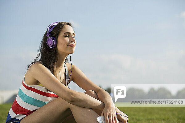 Junge Frau mit Kopfhörern  die an einem sonnigen Tag Musik hört