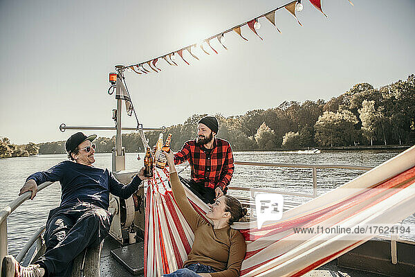 Glückliche Freunde  die auf dem Bug des Bootes sitzen und Bierflaschen anstoßen