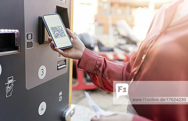 Woman scanning QR code on ticket machine at station