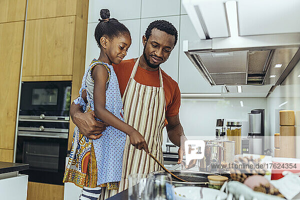 Father looking at daughter preparing food in kitchen
