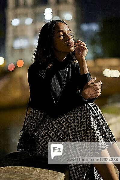 Young woman with eyes closed sitting on footpath at night