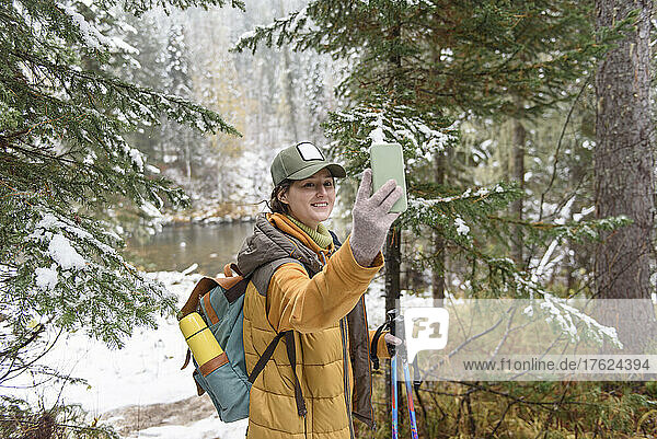 Frau macht Selfie mit Smartphone und steht im Winterwald