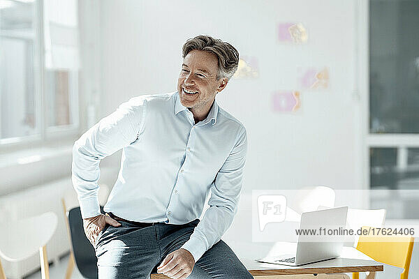 Smiling businessman sitting with hand in pocket at desk
