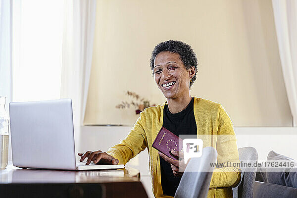 Happy businesswoman with passport using laptop on table at home