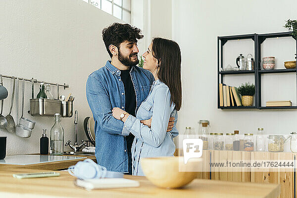 Smiling man embracing girlfriend standing in kitchen at home