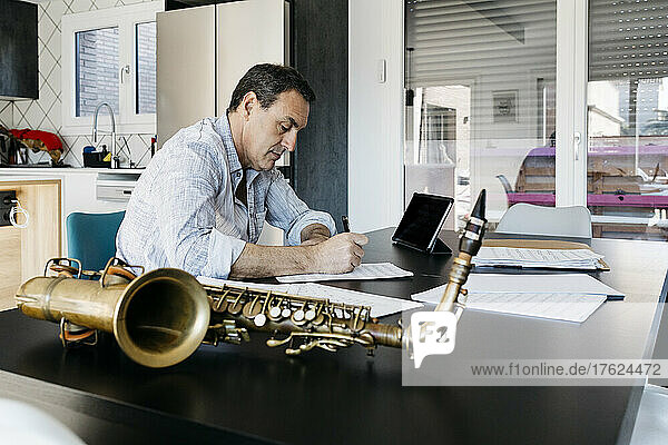 Saxophonist schreibt Noten und steht in der Küche am Tisch