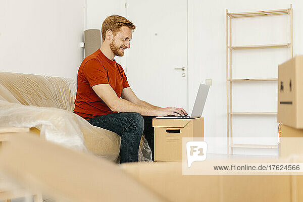Smiling man using laptop sitting on sofa in living room