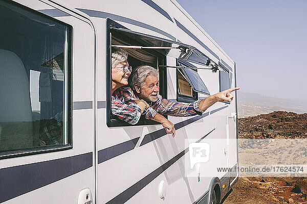Älterer Mann zeigt an einer Frau  die an einem sonnigen Tag durch das Fenster eines Wohnmobils schaut