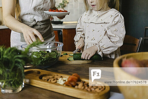 Mädchen schneidet Gurke von Mutter in der heimischen Küche