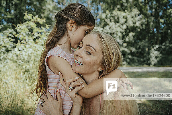 Daughter whispering in mother's ear in nature
