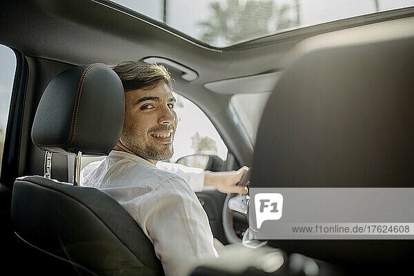 Happy man looking over shoulder sitting in electric car
