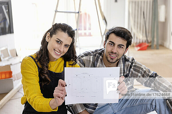 Smiling woman showing floor plan by boyfriend at home