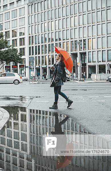 Young woman walking with orange umbrella walking on street