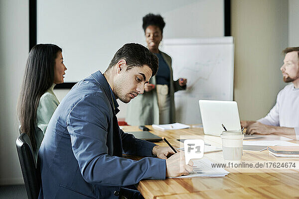 Junger Geschäftsmann macht sich Notizen  während er bei einer Besprechung im Büro am Schreibtisch sitzt