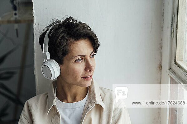 Woman with headphones listening to music by window