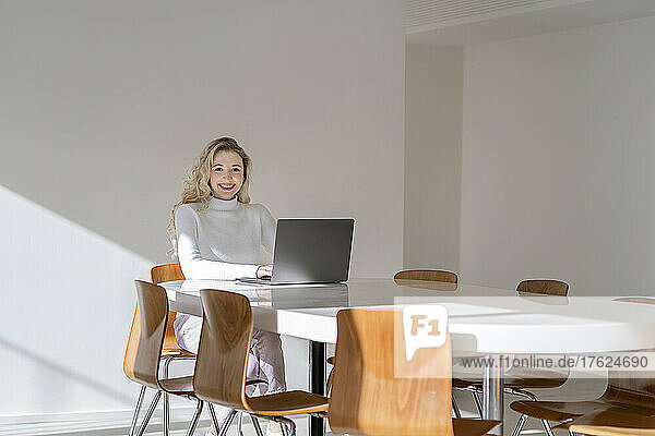 Happy blond woman with laptop sitting at table