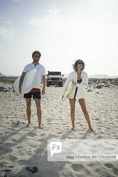 Happy couple standing with surfboard on the beach