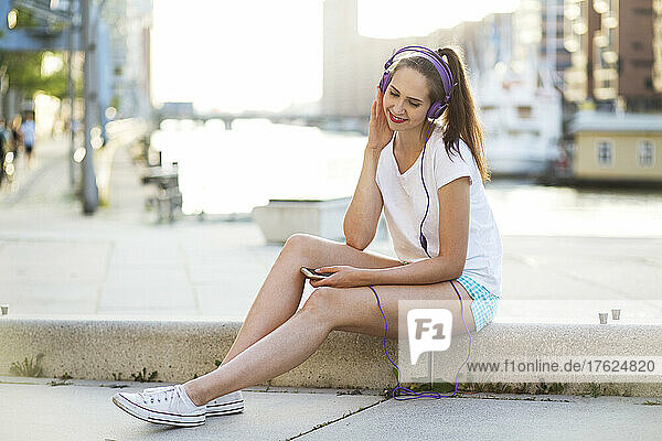 Young woman listening to music with headphones on footpath