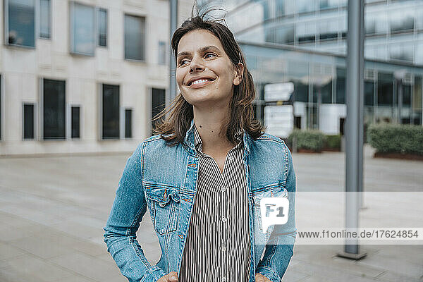 Smiling woman in denim jacket standing in front of building