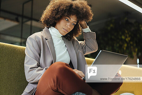 Working woman with hand in hair using laptop at work place