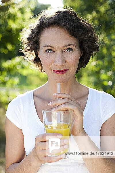 Woman in park with glass of fresh orange juice