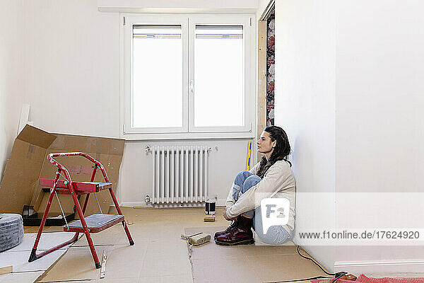 Thoughtful woman sitting on floor at home renovation work