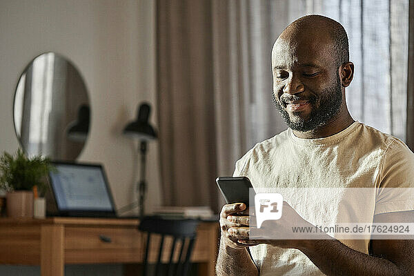 Smiling man using smart phone at home