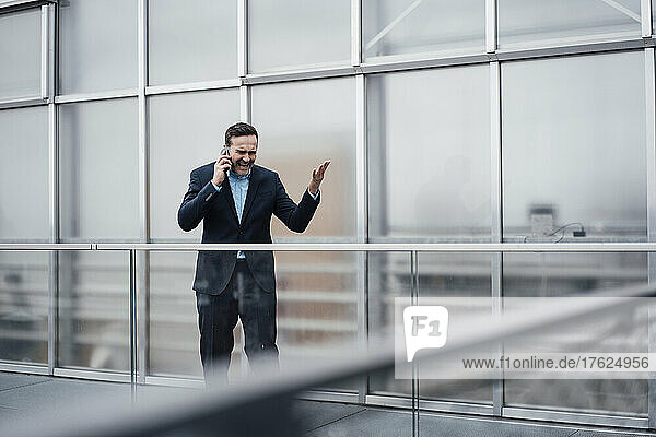 Frustrated businessman arguing on smart phone standing on balcony