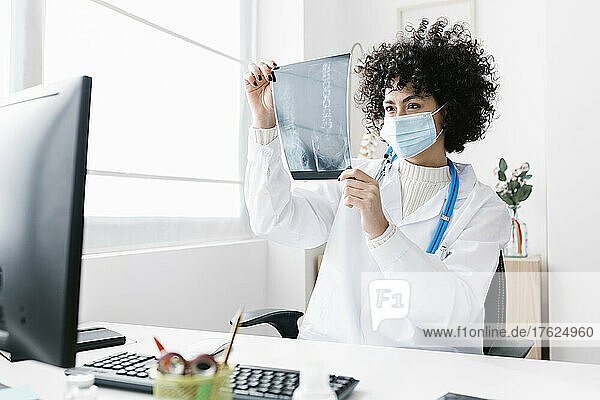 Doctor wearing protective face mask analyzing x-ray report at clinic