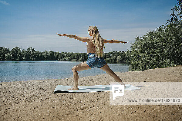 Woman practicing yoga at lakeshore on weekend