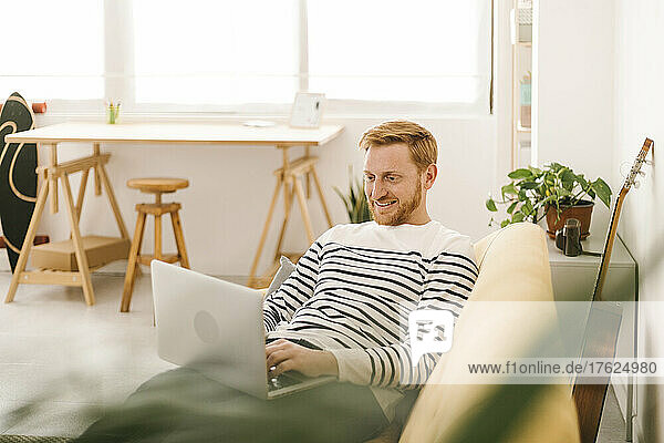 Happy young man using laptop on sofa at home