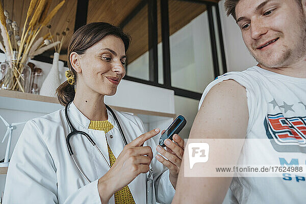 Smiling doctor doing blood glucose test of patient in clinic