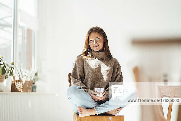 Smiling woman with coffee cup sitting on chair