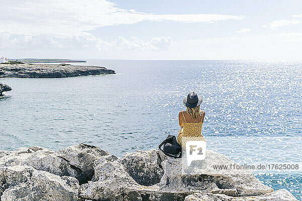 Woman sitting on rock looking at seascape on sunny day  Minorca  Spain