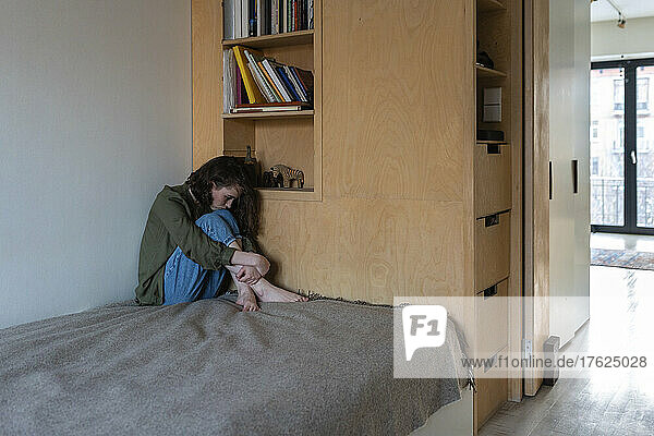 Depressed woman sitting on bed at home