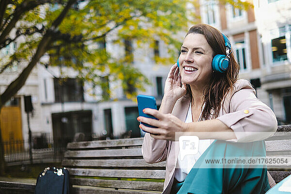 Glückliche Frau hört im Park Musik über Kopfhörer