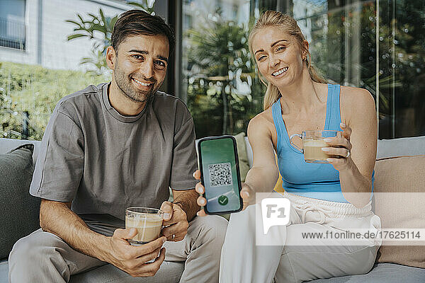 Smiling woman showing green pass on smart phone by man at lounge