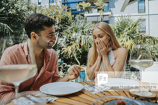 Surprised woman looking at man with engagement ring at outdoor table