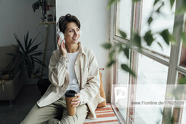 Happy woman with disposable coffee cup listening to music with headphones